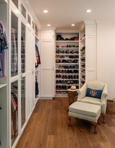 A walk in closet with a chair and shoes.